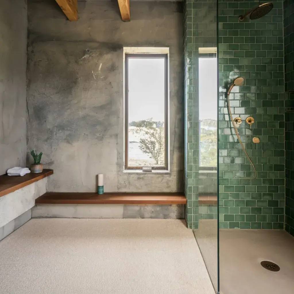 Salle de bain moderne avec douche en carrelage vert, mur texturé, et fenêtre offrant une vue apaisante.