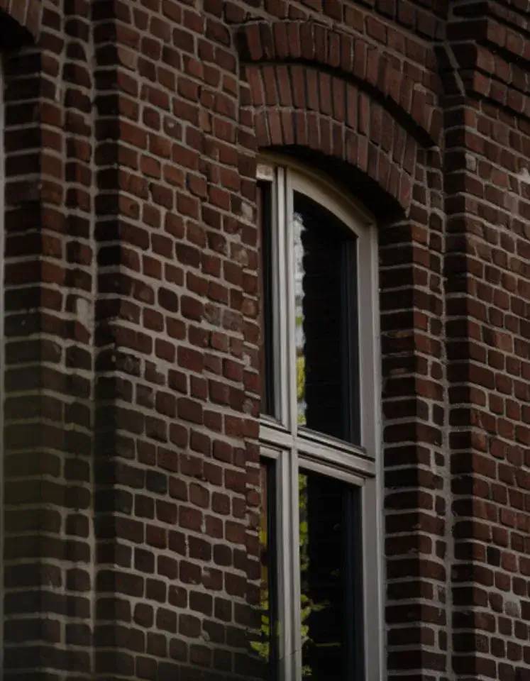 Une fenêtre encadrée de briques rouges, laissant entrevoir des reflets sur le verre.