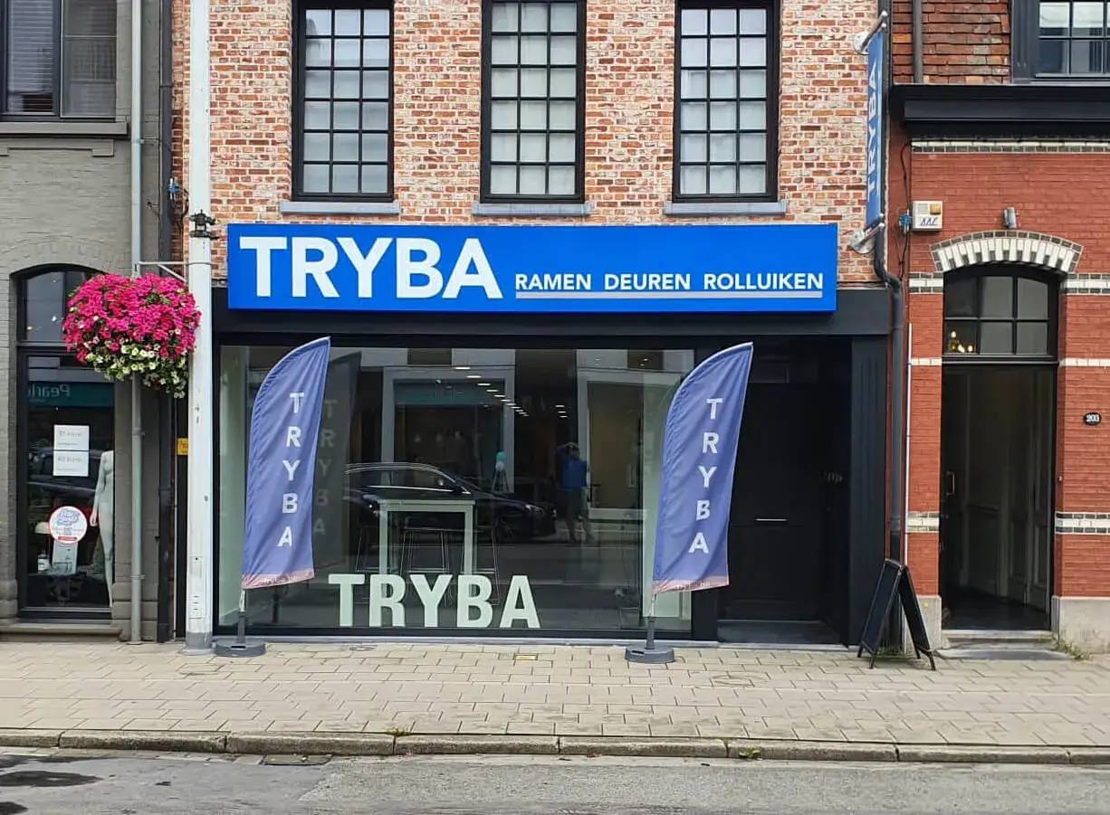 Façade d'un magasin Tryba avec une enseigne bleue et des drapeaux publicitaires, spécialisée dans la vente de fenêtres, portes
