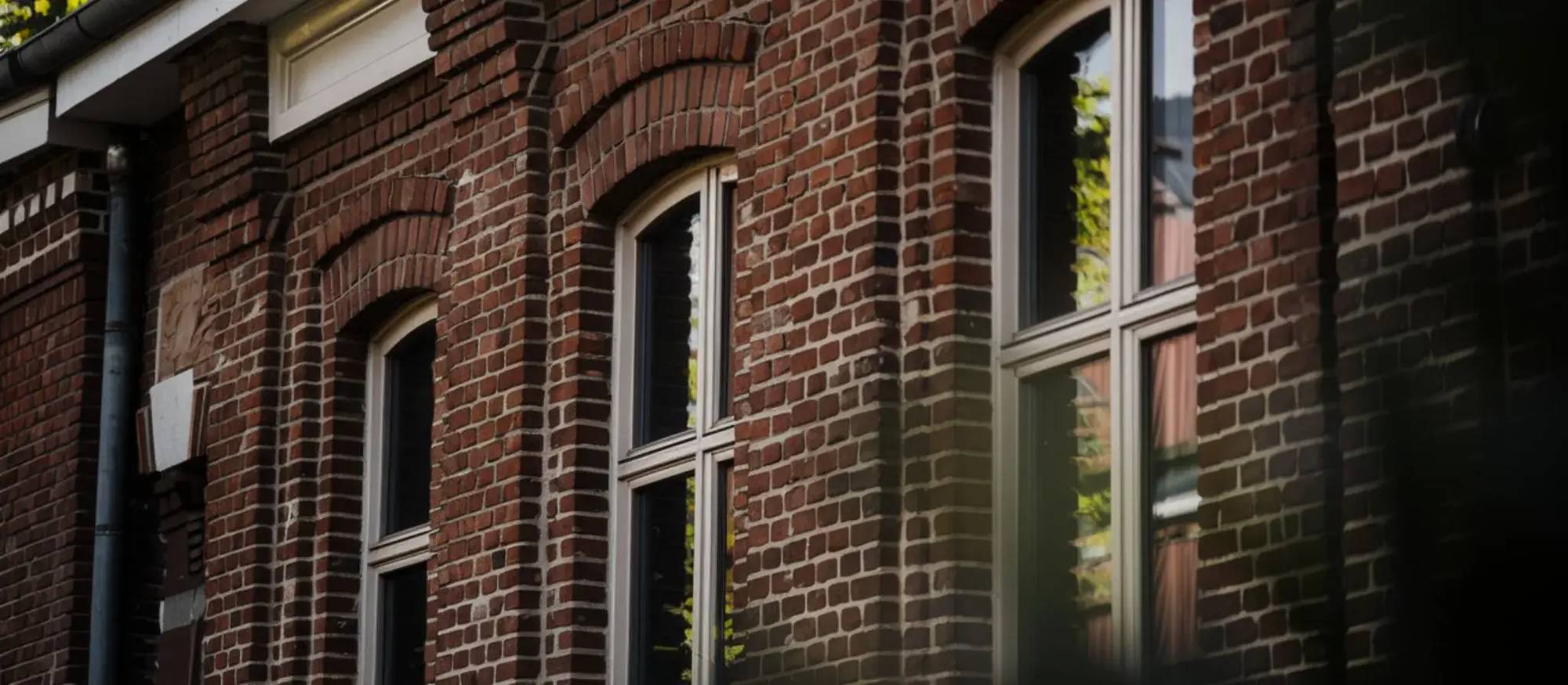 Une façade en briques rouges avec des fenêtres à double vitrage reflétant la lumière naturelle.
