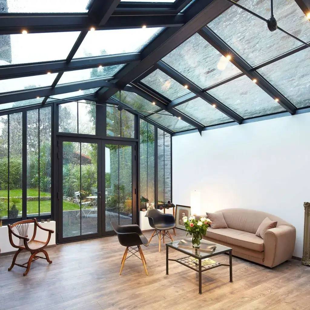 Une véranda moderne avec toit en verre et mobilier élégant, offrant une vue sur un jardin verdoyant.