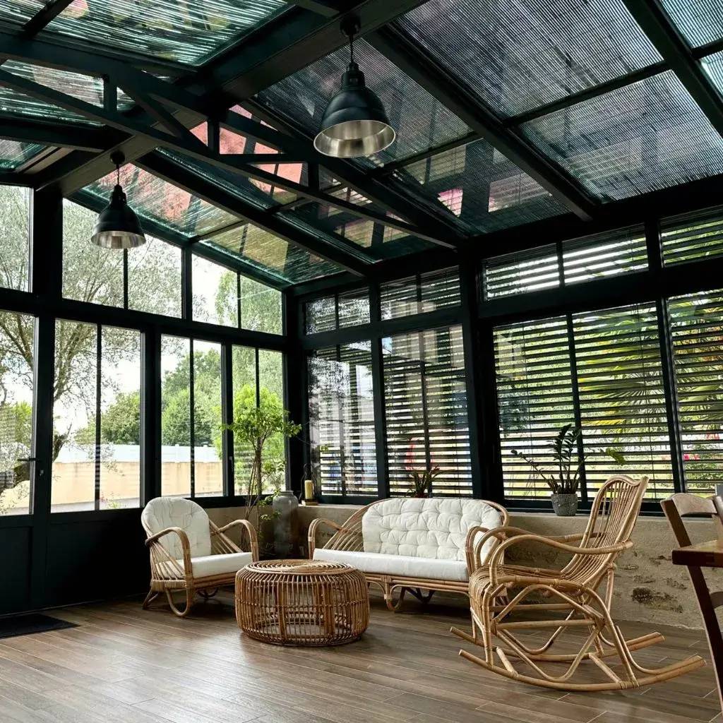 Une véranda lumineuse et moderne avec des meubles en rotin confortables, offrant une vue sur le jardin extérieur.