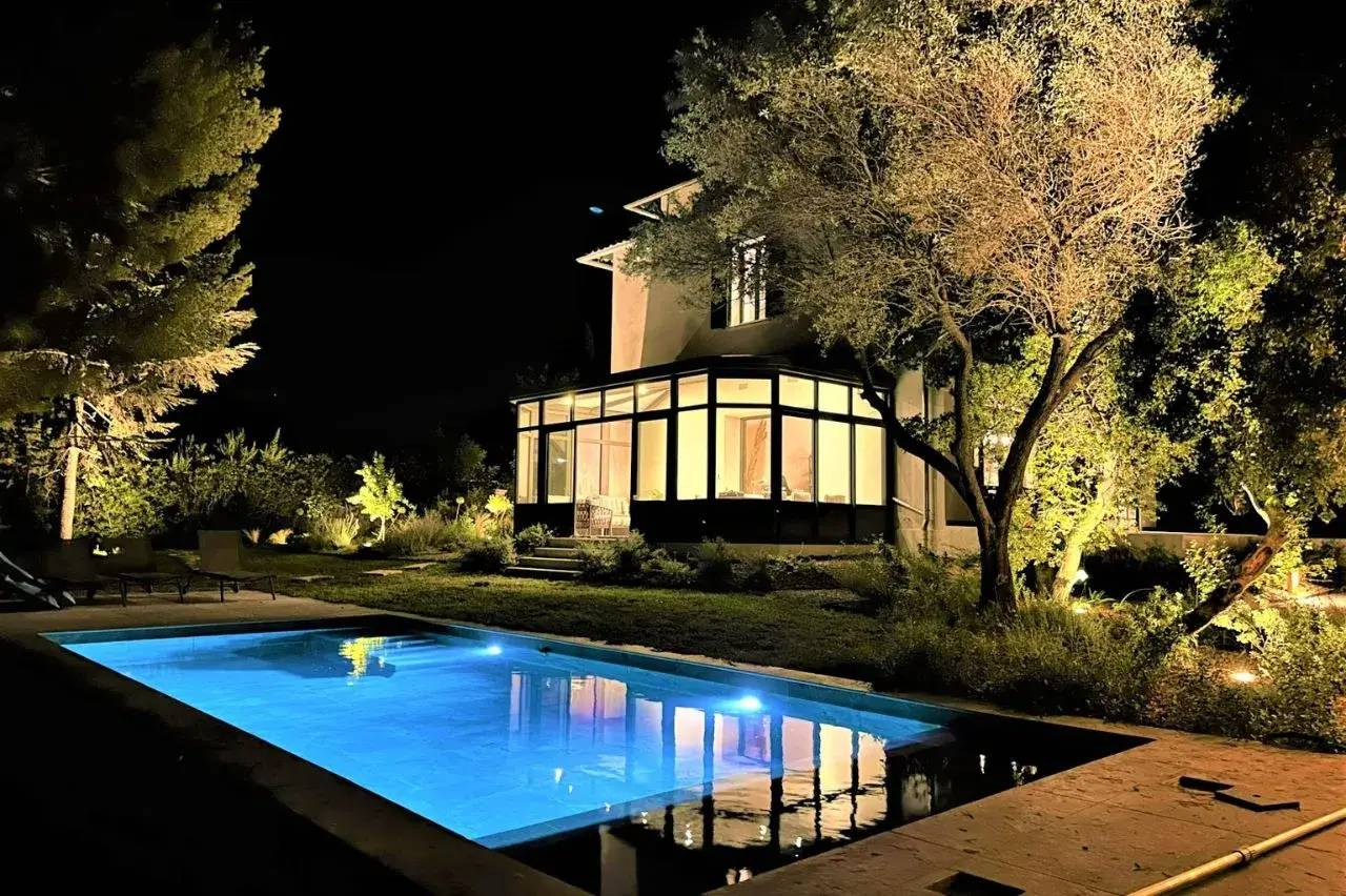 Une maison moderne illuminée de nuit avec une piscine scintillante et un jardin verdoyant.