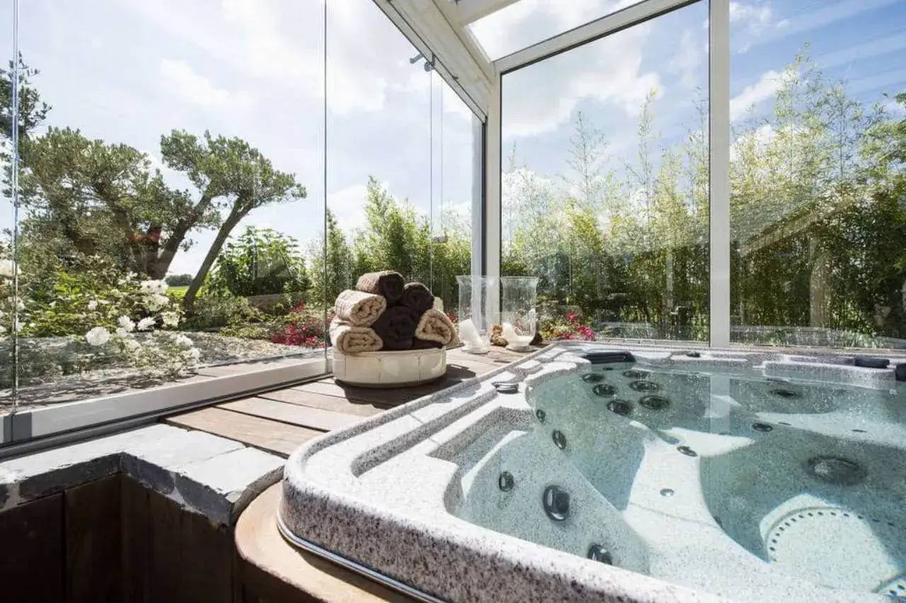 Un jacuzzi luxueux est installé dans une véranda lumineuse avec vue sur le jardin.