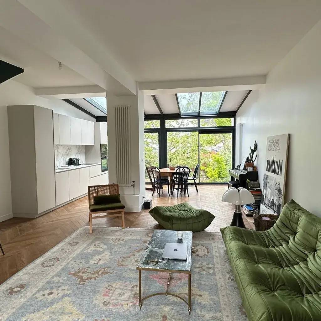 Un salon moderne et lumineux avec un canapé vert, une table basse en marbre, et une grande baie vitrée donnant sur une terrasse.