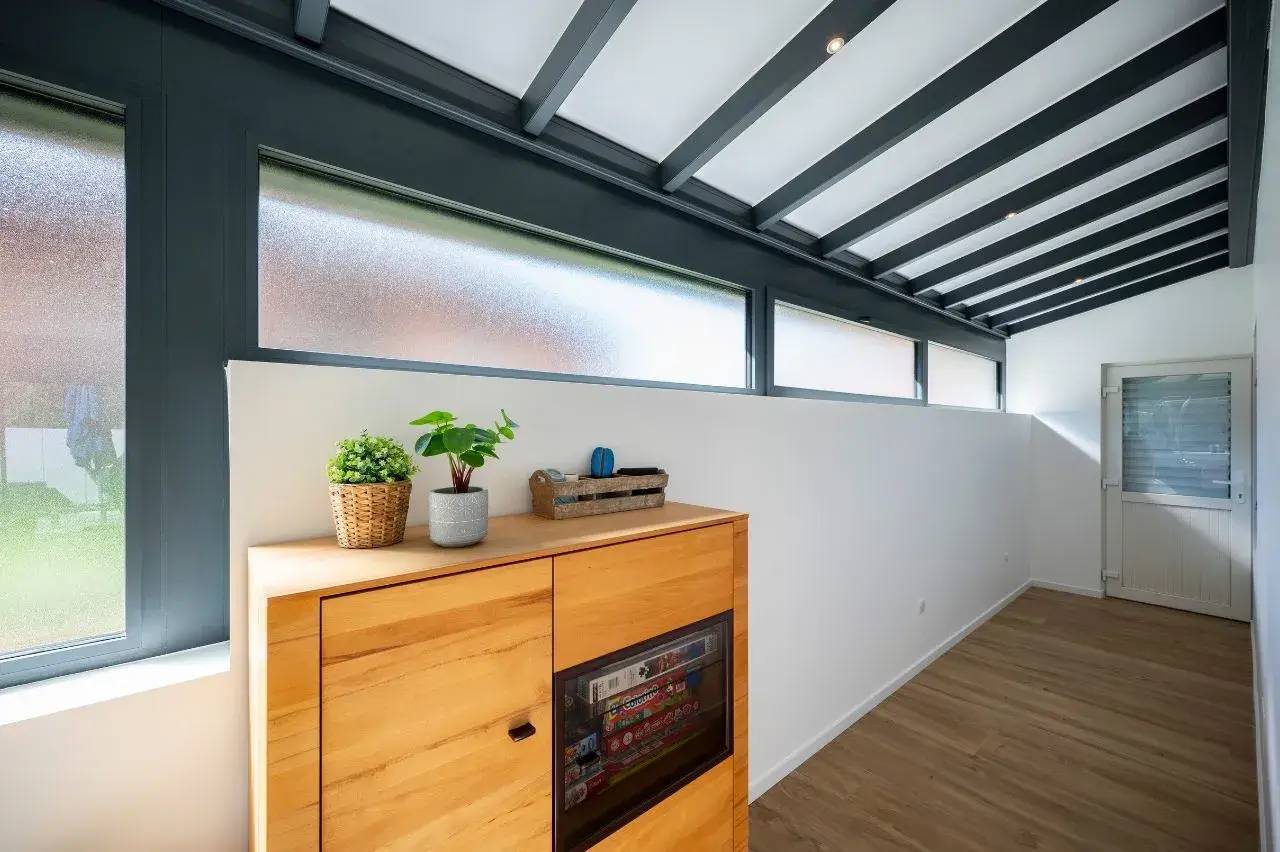 Un couloir lumineux avec un plafond en poutres apparentes et un meuble en bois décoré de plantes, baigné de lumière naturelle par des fenêtres