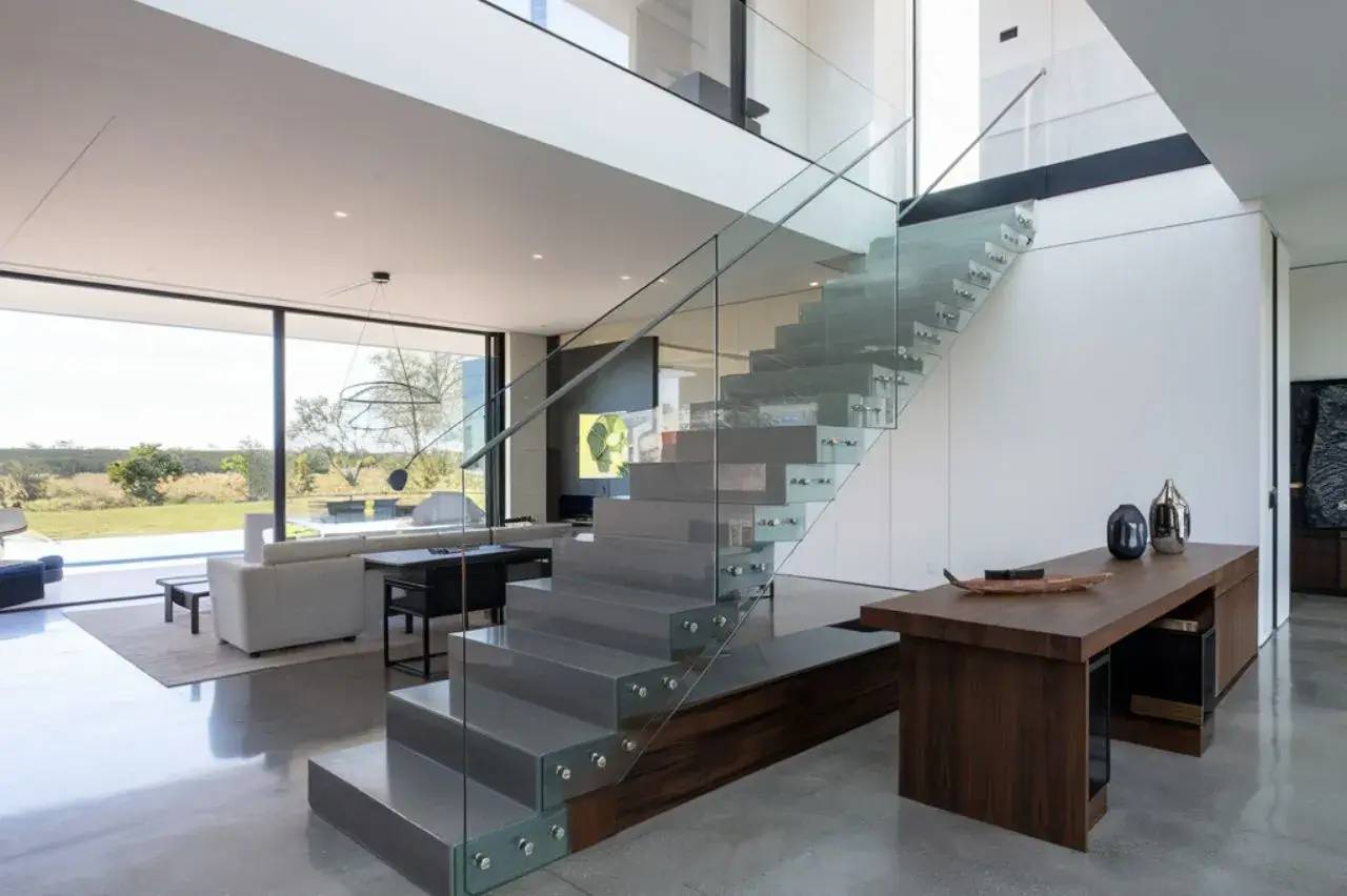 Un intérieur moderne avec un escalier en verre élégant et un salon lumineux donnant sur un paysage verdoyant.