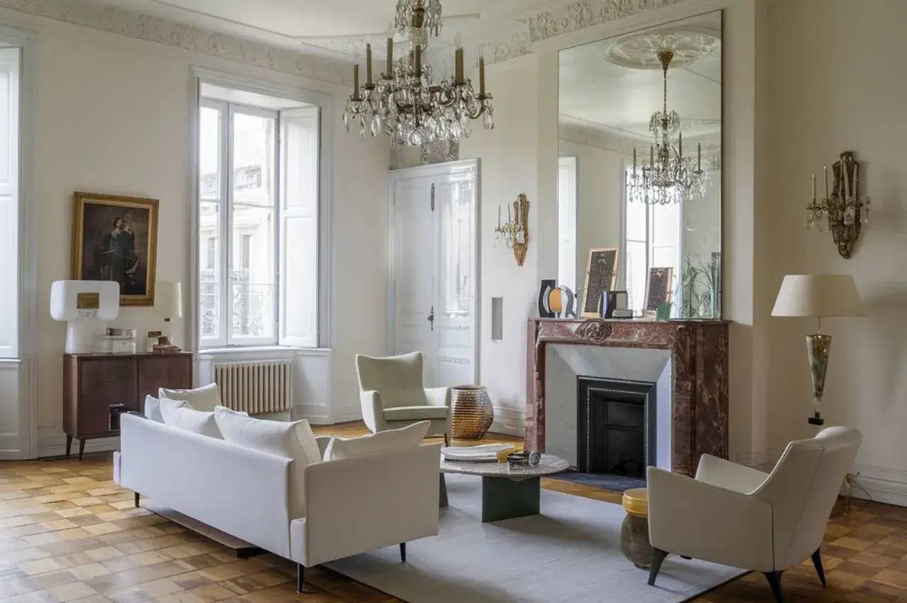 Un salon élégant et lumineux avec des canapés blancs, un parquet en bois, une cheminée en marbre et un grand miroir.