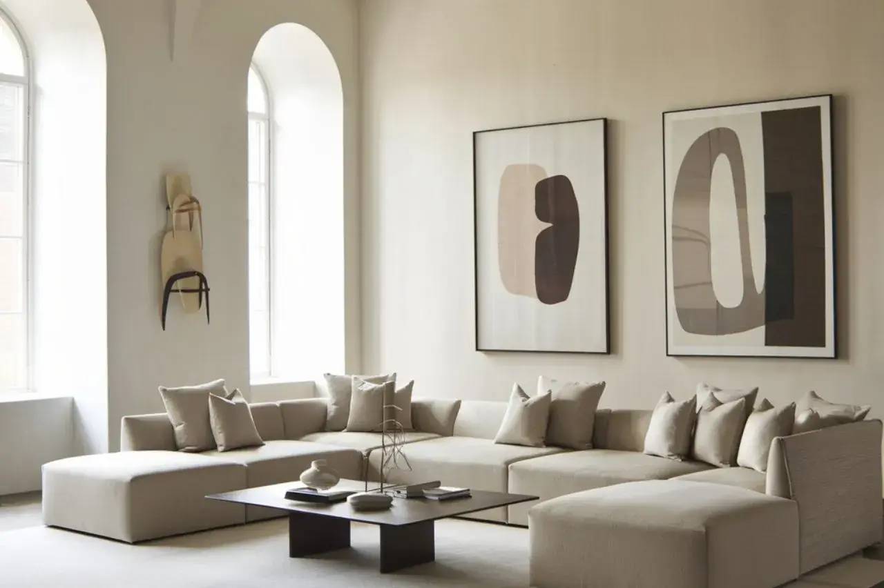 Un salon moderne et épuré avec un canapé en L beige, des œuvres d'art abstraites aux murs et une table basse élégante.