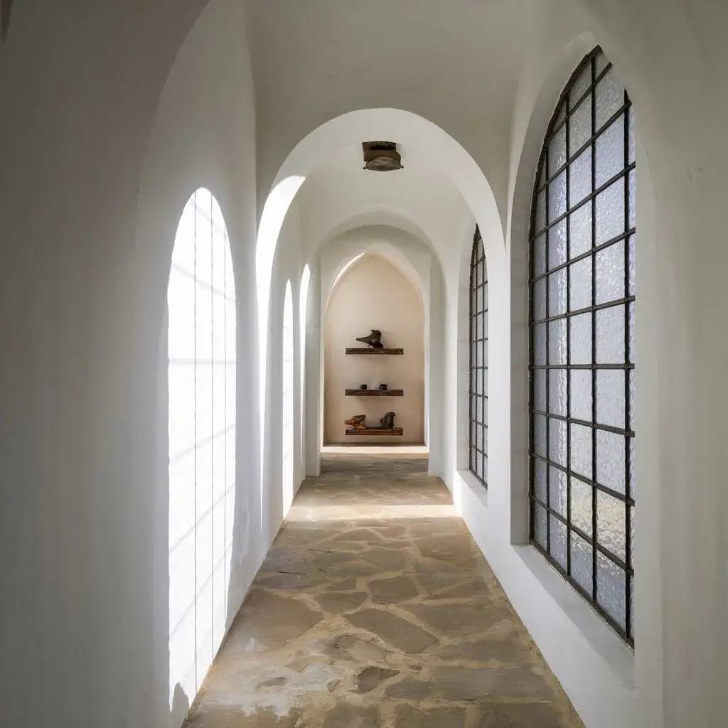 Un couloir lumineux et épuré avec des arches blanches, des fenêtres à carreaux et des étagères murales en bois accueillant des