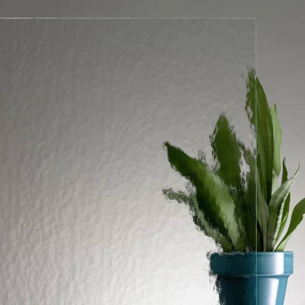 Une plante verte dans un pot bleu apparaît floue derrière une vitre texturée transparente.