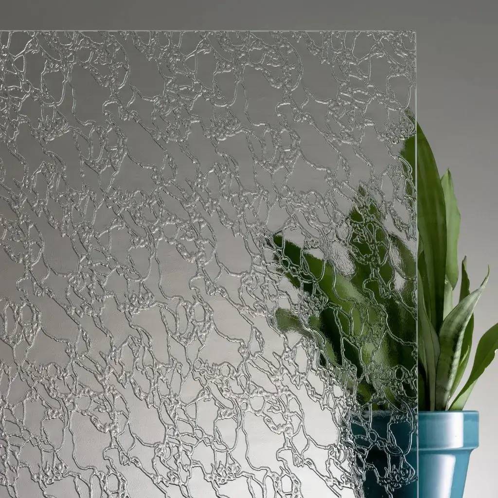 Un panneau de verre texturé avec un motif organique, partiellement flou, révèle les feuilles vertes d'une plante en arrière-plan.