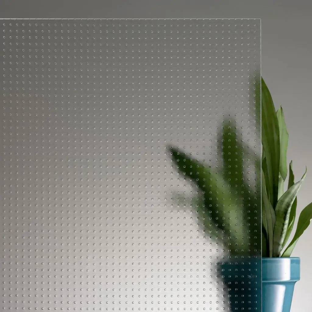 Un panneau de verre à motifs carrés partiellement translucide, derrière lequel se trouve une plante verte en pot.
