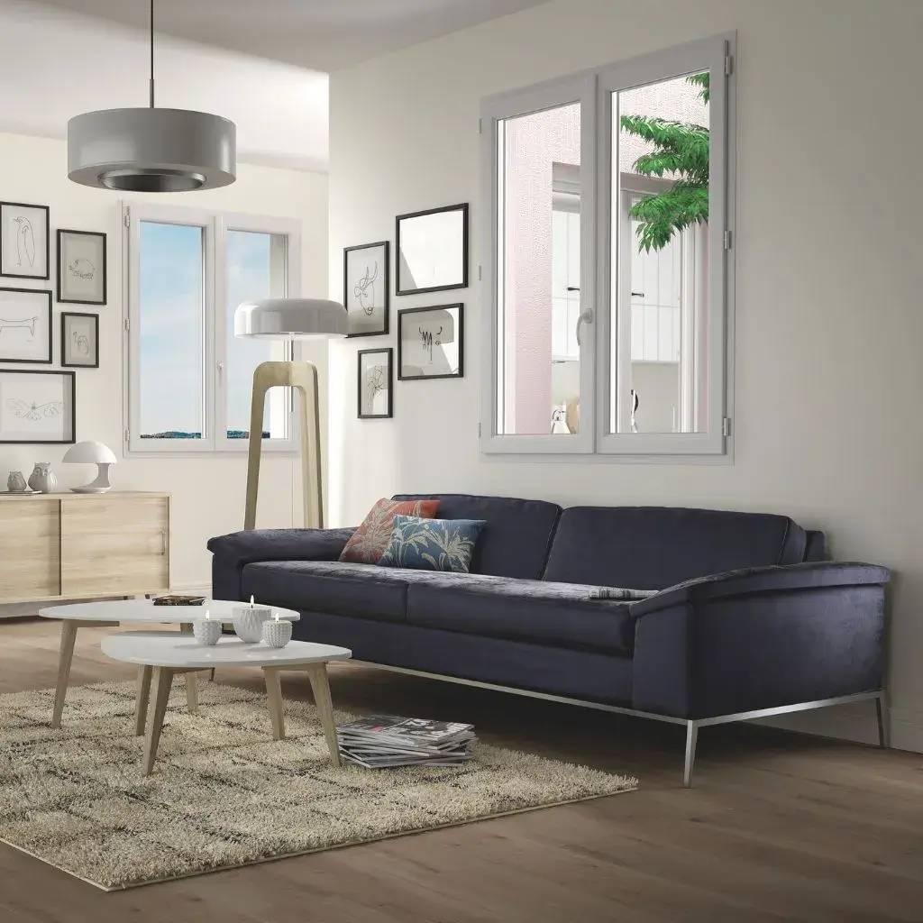 Un salon moderne et lumineux avec un canapé bleu foncé, des tables basses blanches, et un mur décoré de cadres artistiques.
