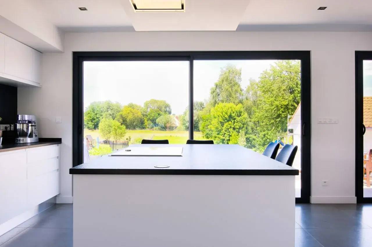 Cuisine moderne avec grande baie vitrée offrant une vue sur un jardin verdoyant.