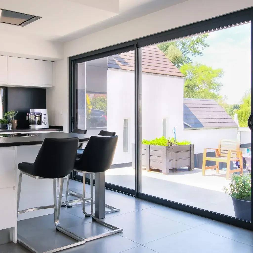 Une cuisine moderne avec un îlot central et de grandes baies vitrées donnant sur une terrasse ensoleillée.