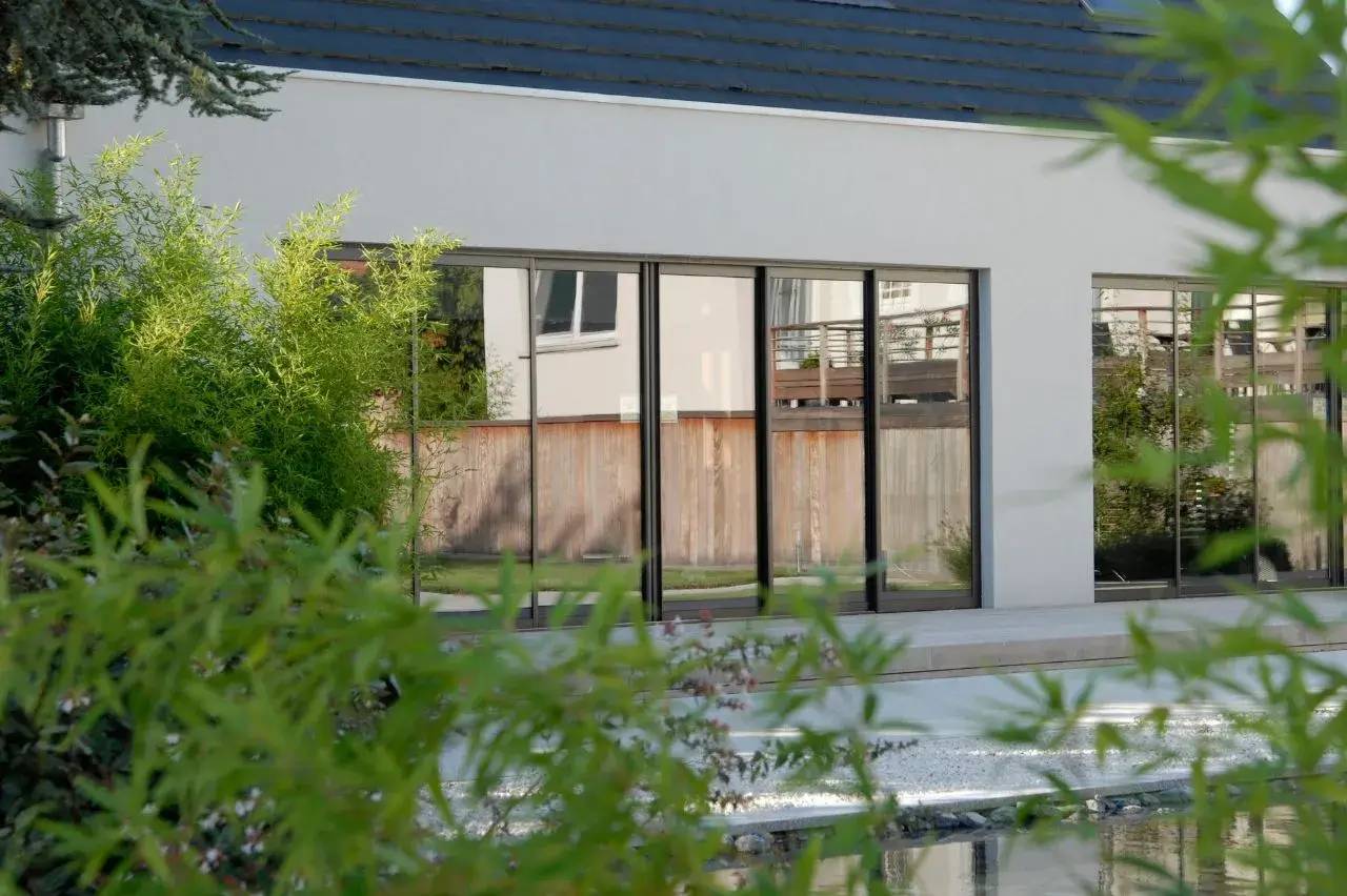 La photo montre une maison moderne avec de grandes baies vitrées, entourée de verdure.