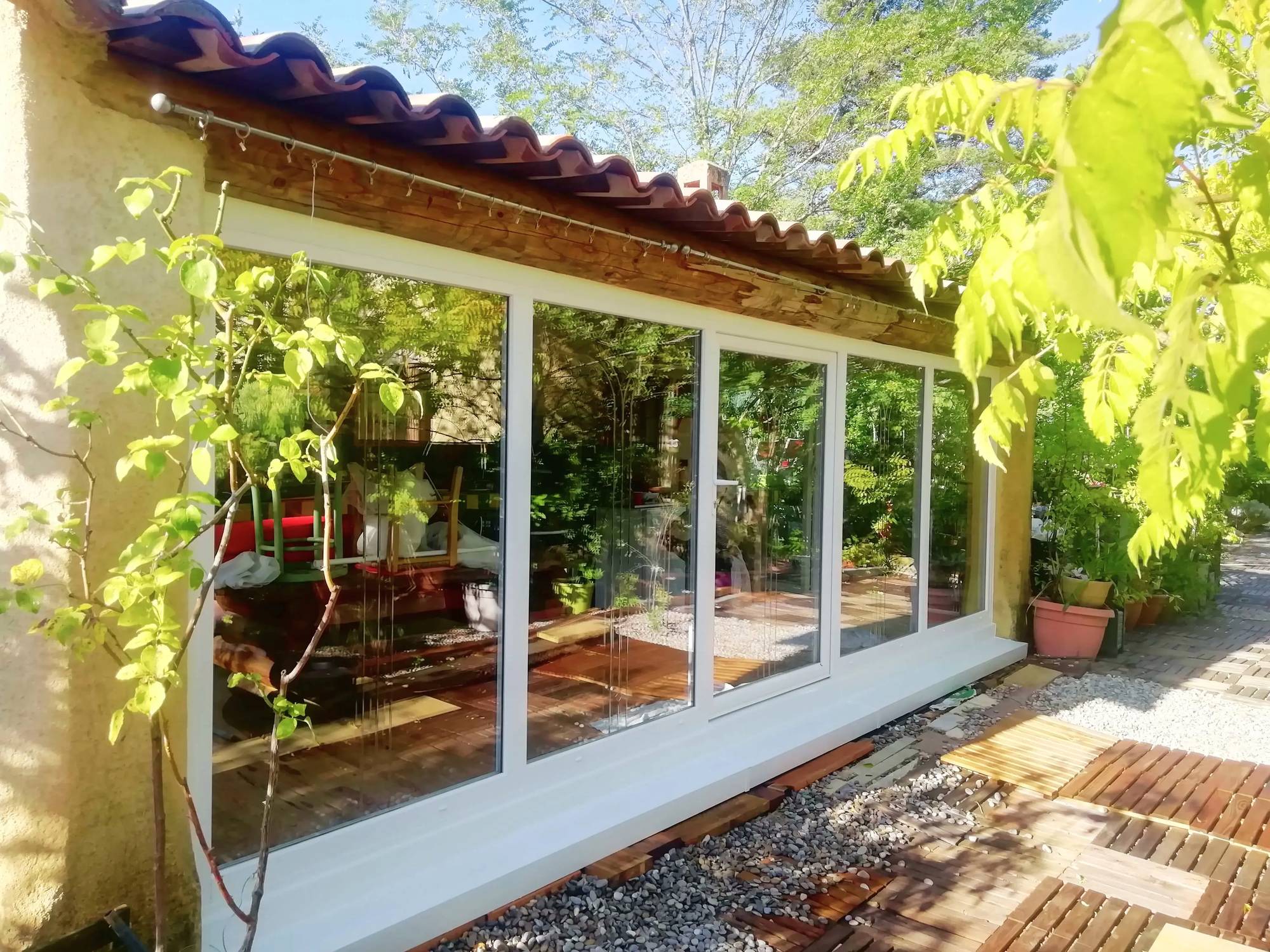 Une véranda lumineuse avec de grandes baies vitrées entourée de verdure et de plantes en pots.