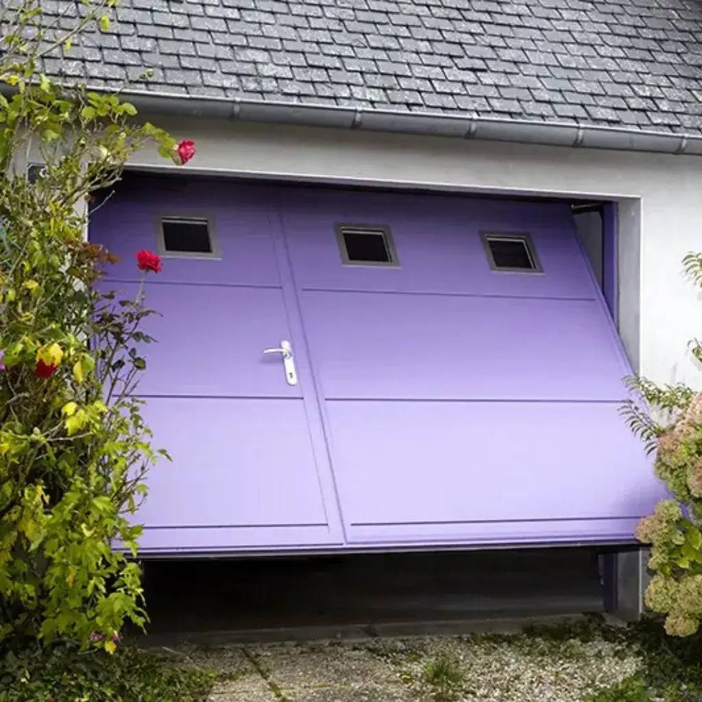 Une porte de garage violette ouverte, entourée de verdure, avec trois petites fenêtres rectangulaires.
