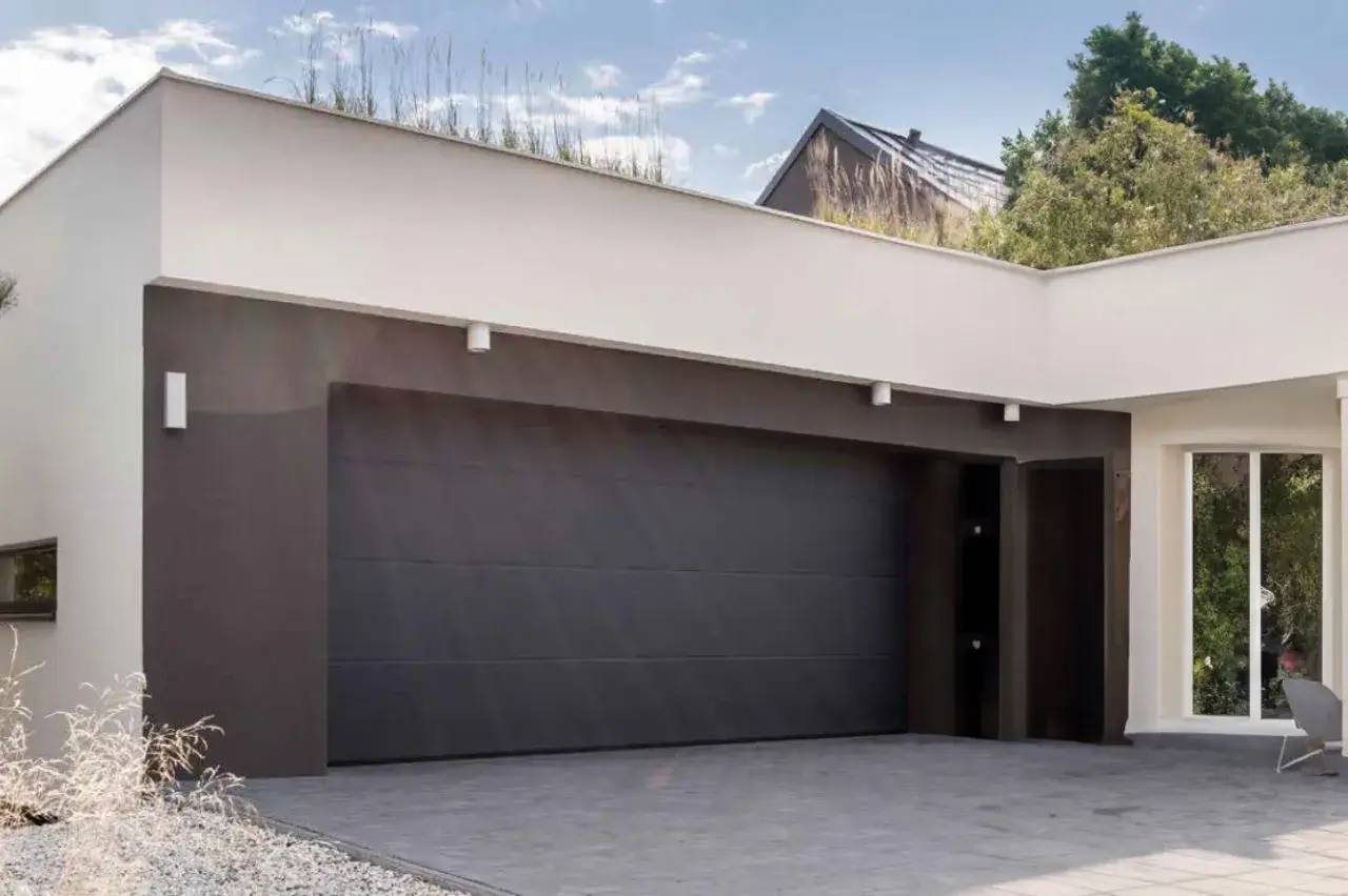 Garage moderne avec une grande porte noire, entouré de végétation et d'une architecture épurée.