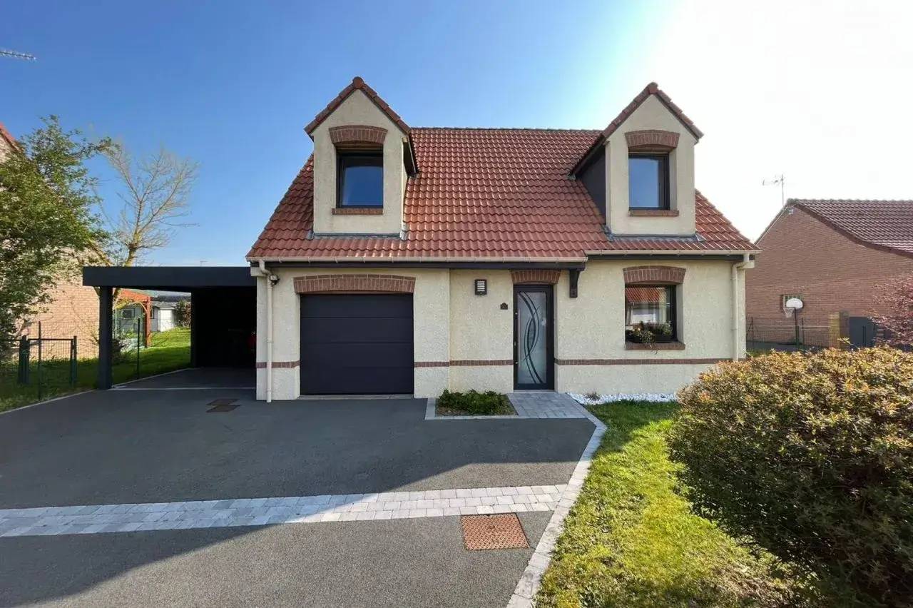 Maison moderne avec toit en tuiles rouges, garage intégré, et allée pavée dans un cadre résidentiel.